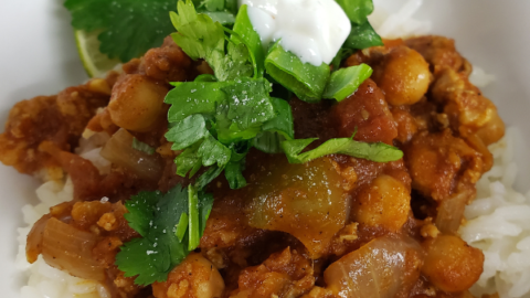 Bowl of rice with chickpeas and ground chicken in a tomato sauce with green cilantro and yogurt topping