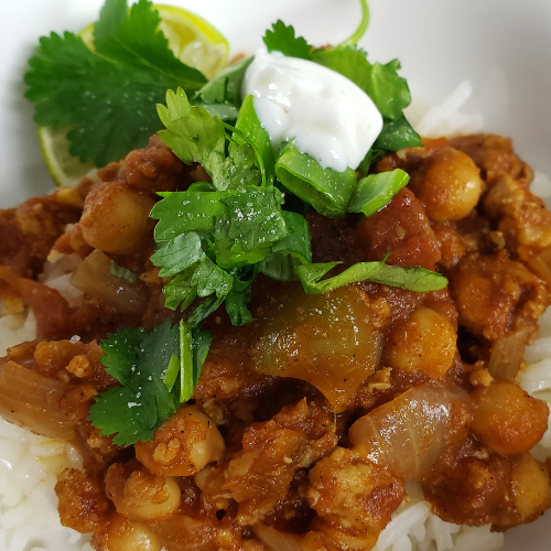 Bowl of rice with chickpeas and ground chicken in a tomato sauce with green cilantro and yogurt topping