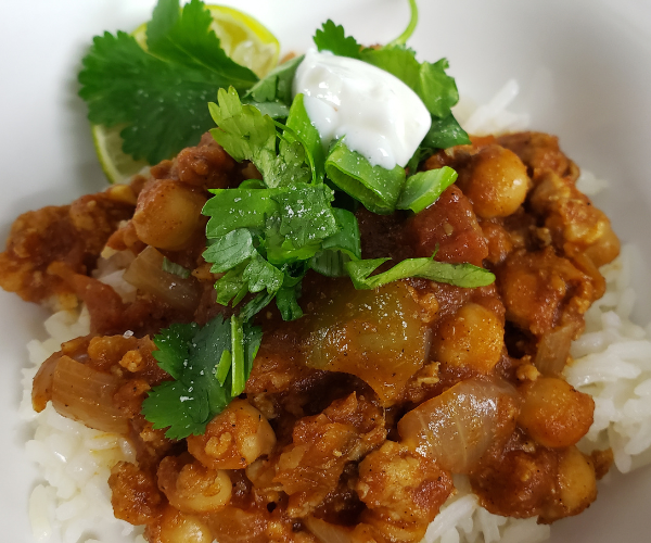 Bowl of rice with chickpeas and ground chicken in a tomato sauce with green cilantro and yogurt topping