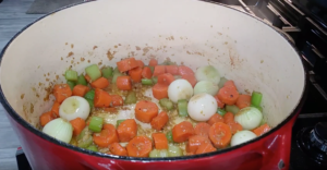 Carrots celery and onions cooking in red cast iron pot