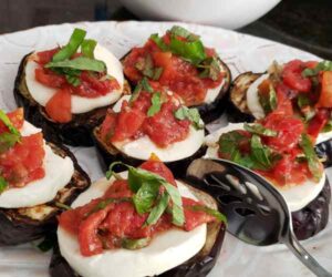 Red rossted tomatoes,green basil, and white cheese on top of roasted eggplant slices