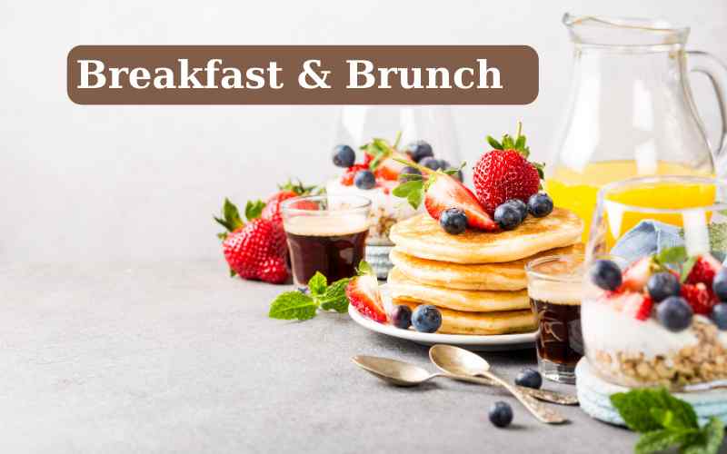 A colorful breakfast buffet with a stack of pancakes with bright red strawberries and blueberries on top