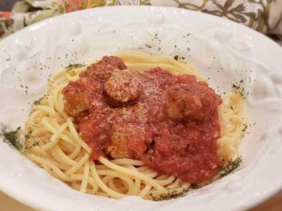 White Bowl filled with red pasta sauce with meatballs and sausage over spaghetti