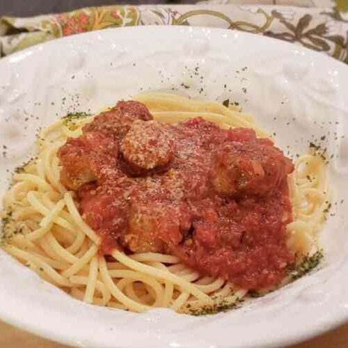 White Bowl filled with red pasta sauce with meatballs and sausage over spaghetti